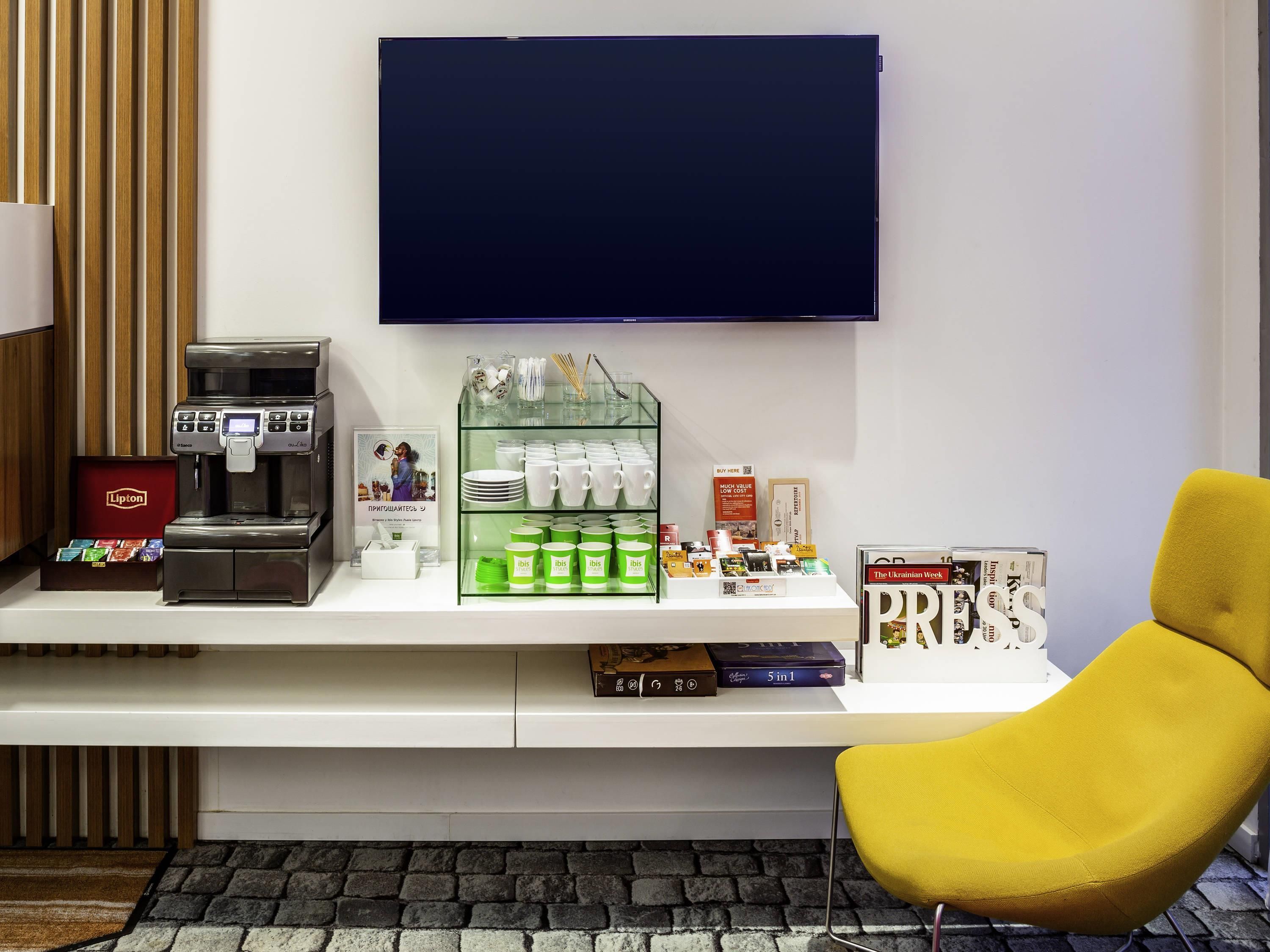 Una estación de café moderna con una cafetera, una colección de tazas y una silla amarilla.