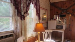 A cozy room with a wooden ceiling, a white table with a lamp, a white chair, a small white table, and a microwave on a wooden table. - Lake Winnipesaukee Motel (Laconia)