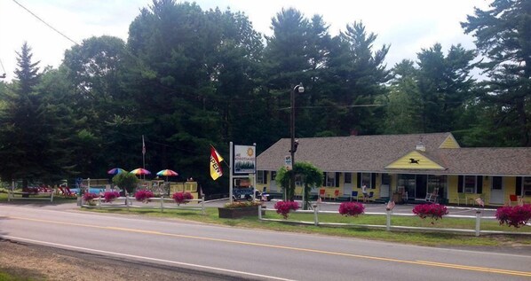 A motel with a yellow facade, a covered parking area, and a sign indicating it's open. - Lake Winnipesaukee Motel (Laconia)