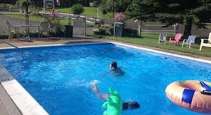 A swimming pool with a person swimming, a green inflatable toy, and a pink inflatable float. - Lake Winnipesaukee Motel (Laconia)