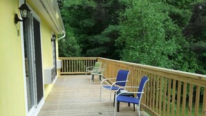 A wooden deck with a yellow wall, two blue chairs, and a wooden railing. - Lake Winnipesaukee Motel (Laconia)