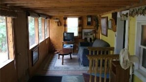A cabin interior with a wooden floor, a television, a dining table, and a window overlooking greenery. - Lake Winnipesaukee Motel (Laconia)