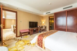Quarto de hotel com uma cama, uma mesa de trabalho com televisão, uma cadeira, um candeeiro e um guarda-roupa.