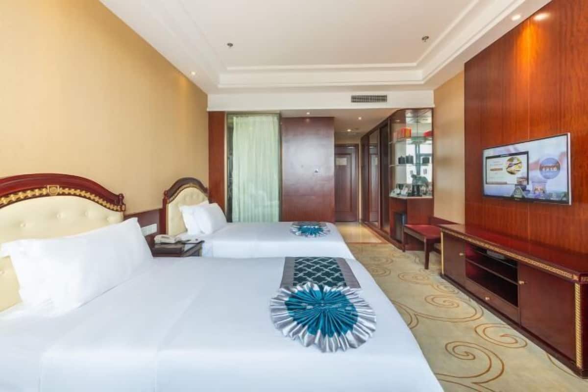 Quarto de hotel com duas camas, televisão, escrivaninha e espelho.