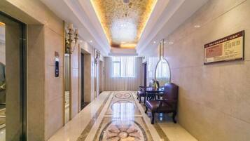 A hotel lobby with a polished marble floor, a decorative ceiling, and a seating area with leather chairs.