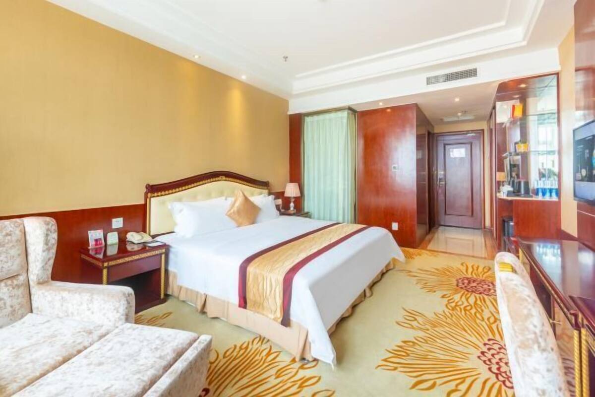 Quarto de hotel com cama, cadeira, mesa de cabeceira, televisão e porta para outro cômodo.
