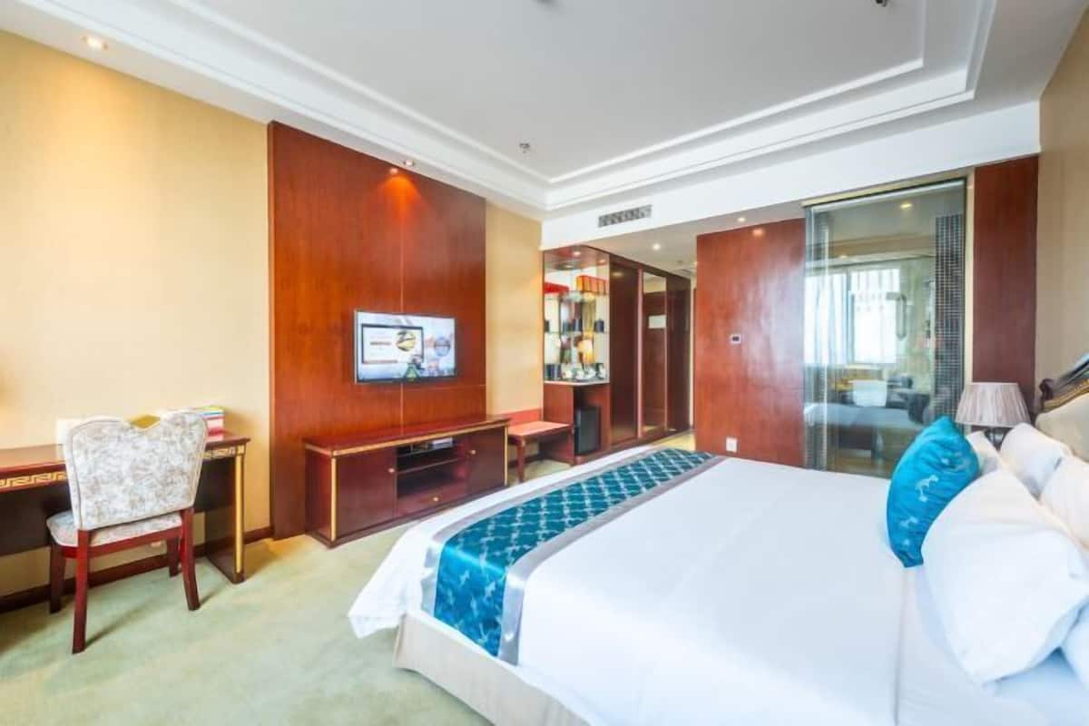 Quarto de hotel com uma cama grande, uma escrivaninha, uma cadeira, uma televisão e chuveiro em box de vidro.