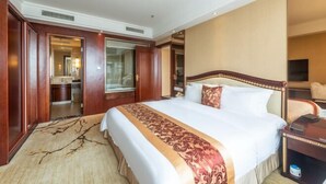 Ein Hotelzimmer mit einem großen Bett, einem Holzkopfstück, einem Nachttisch und Blick ins Badezimmer.
