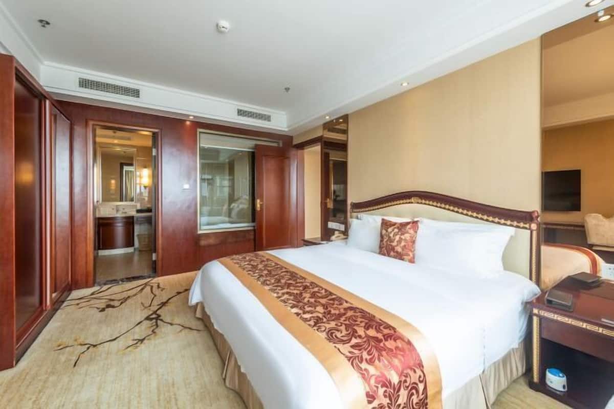 Quarto de hotel com uma cama grande, cabeceira de madeira, mesa de cabeceira e vista para o banheiro.