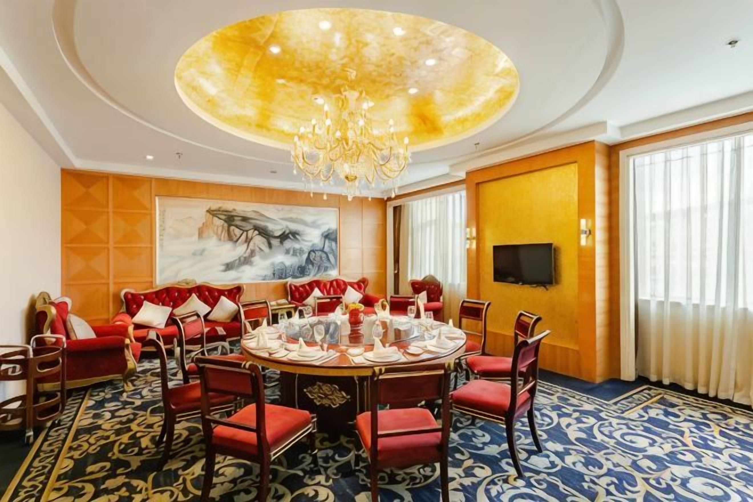 A conference room with a round table, red chairs, a chandelier, a large painting, and a television on the wall.