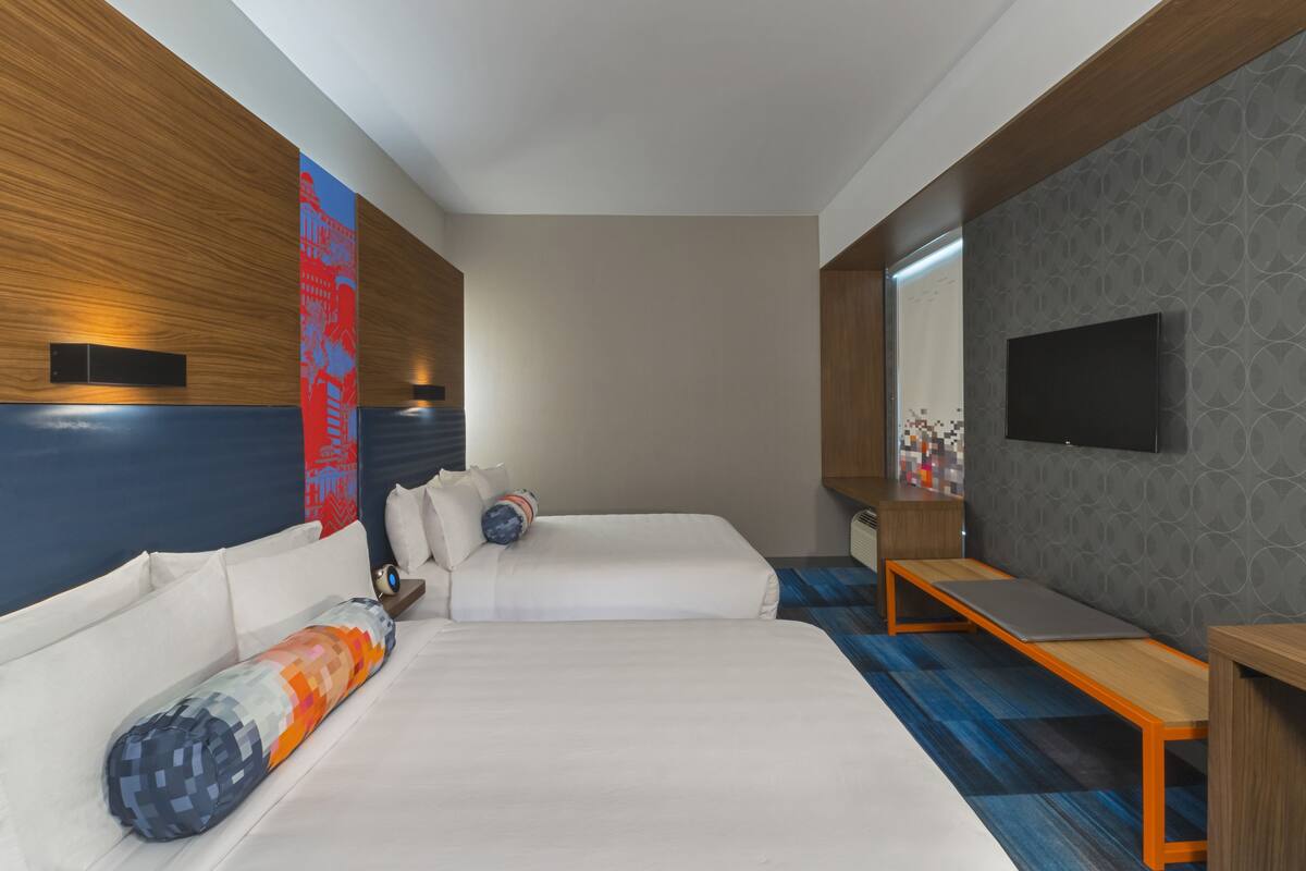 A hotel room with two beds, a desk, a TV, and a large window.