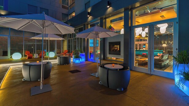 An outdoor seating area with umbrellas, round tables, and comfortable seating. - Aloft by Marriott College Station (College Station)