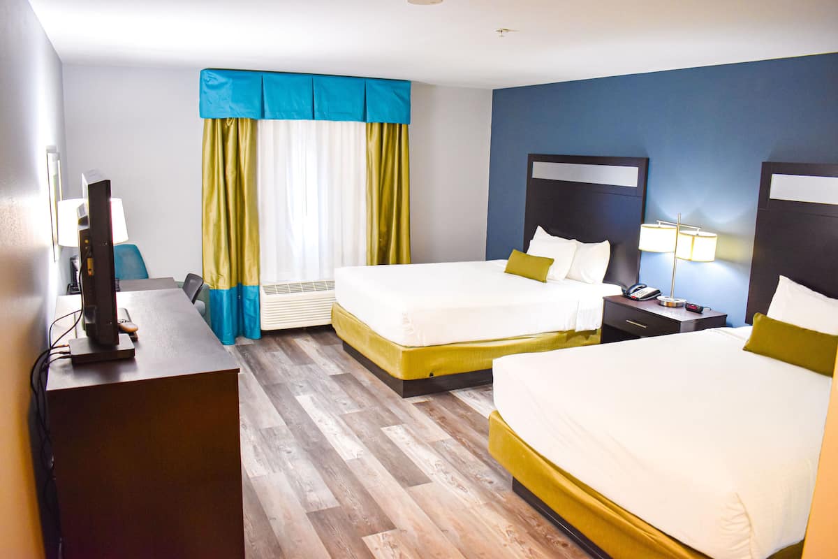 Ein Hotelzimmer mit zwei Betten, einem Schreibtisch mit Computer und einem Fenster mit Vorhängen.