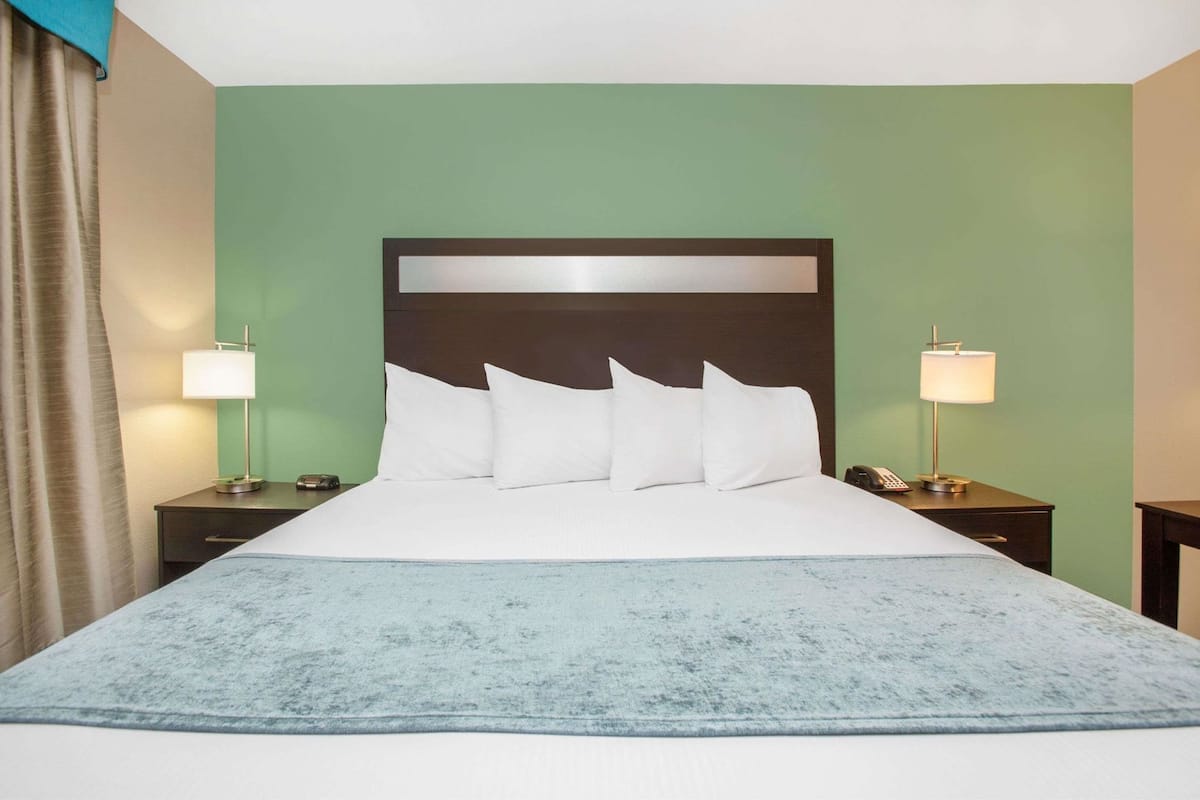 Ein Hotelzimmer mit einem großen Bett, zwei Nachttischen mit Lampen, einem Kopfteil und einer blauen Tagesdecke.