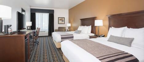 A hotel room with two beds, a desk, a TV, and a window with curtains.