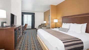 A hotel room with a large bed, a desk with a television, a chair, and a desk lamp.