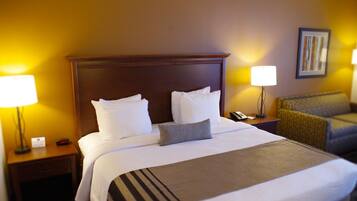 A hotel room with a large bed, two bedside lamps, a nightstand, a chair, and a framed picture on the wall.