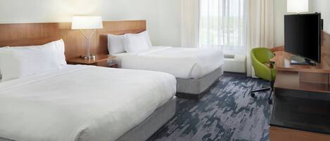 A hotel room with two beds, a desk with a television, and a green chair.