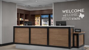 A hotel reception area with a wooden reception desk, a wall sign reading "WELCOME TO THE LONE STAR STATE," and a "Hilton Honors" sign. - Hampton Inn & Suites Georgetown/Austin North (Georgetown)
