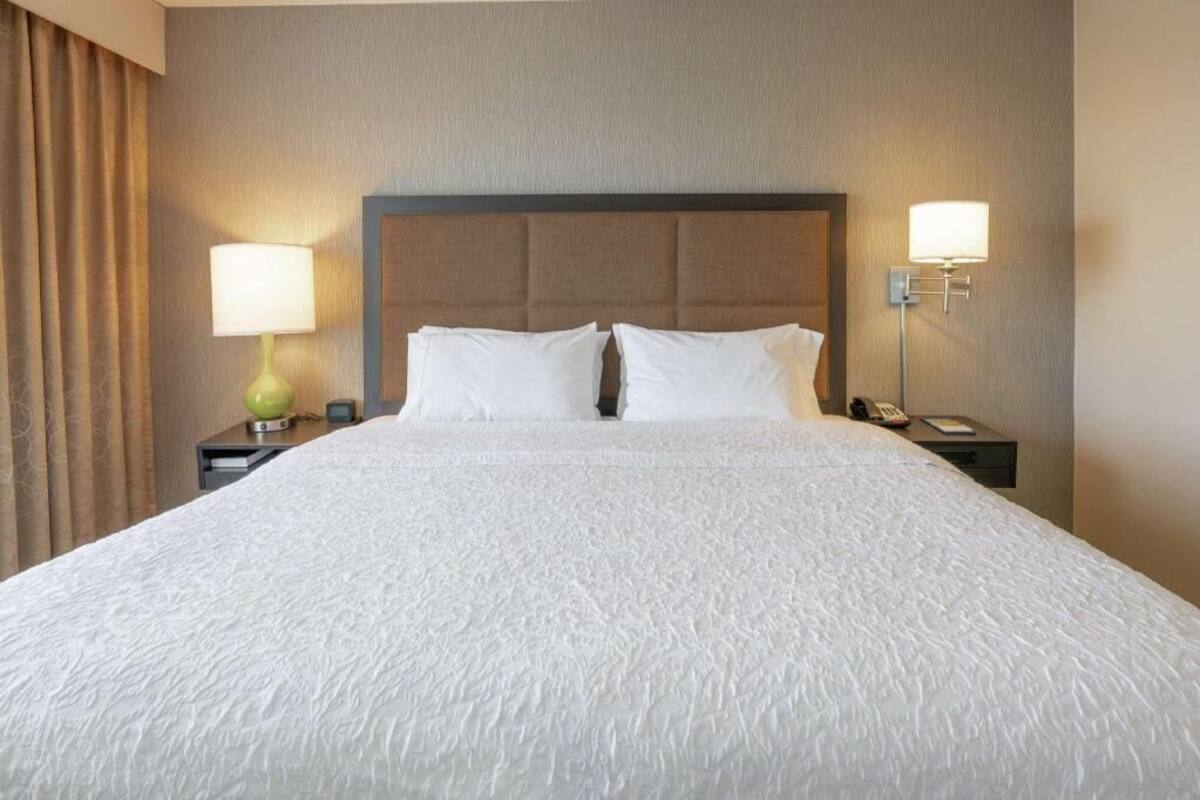A hotel room with a large bed, two bedside tables, a headboard, and two wall-mounted lamps.