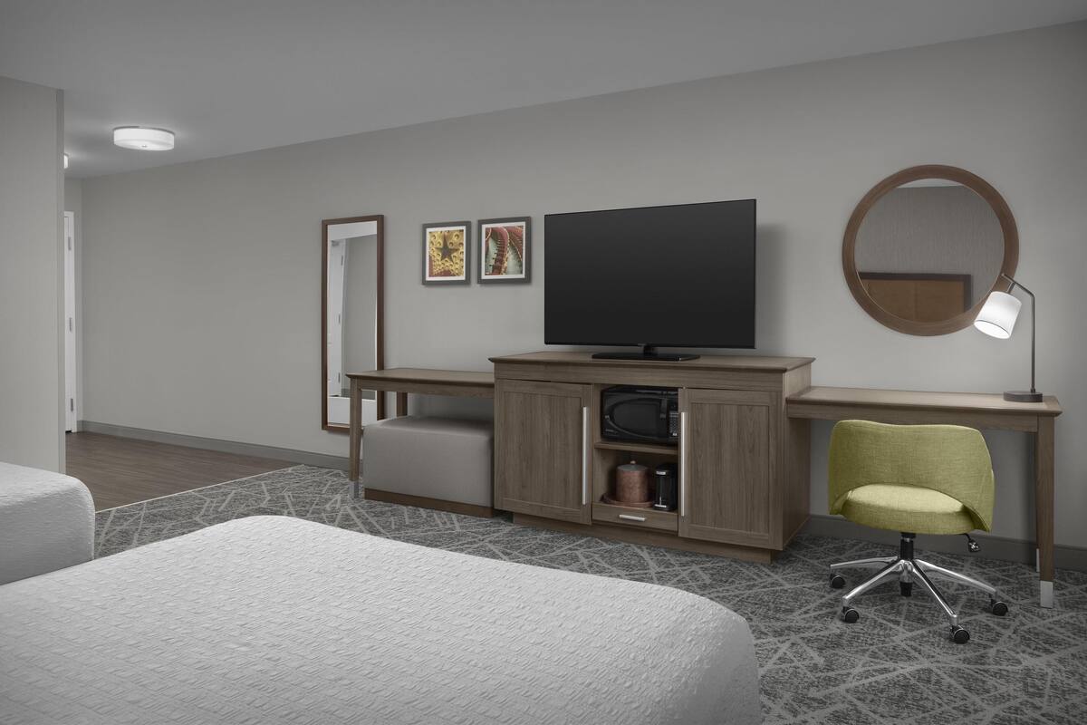 Quarto de hotel com cama, escrivaninha, televisão de tela plana, cadeira, espelho redondo e abajur.