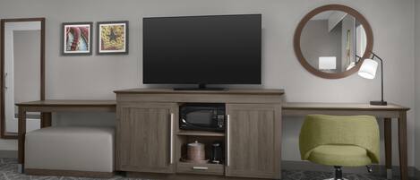 A hotel room with a bed, a desk with a television, a green office chair, a microwave, and a small cabinet.