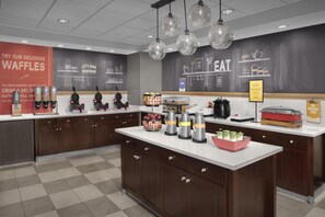 A modern kitchen with waffle stations, coffee makers, and a chalkboard wall with cooking illustrations.