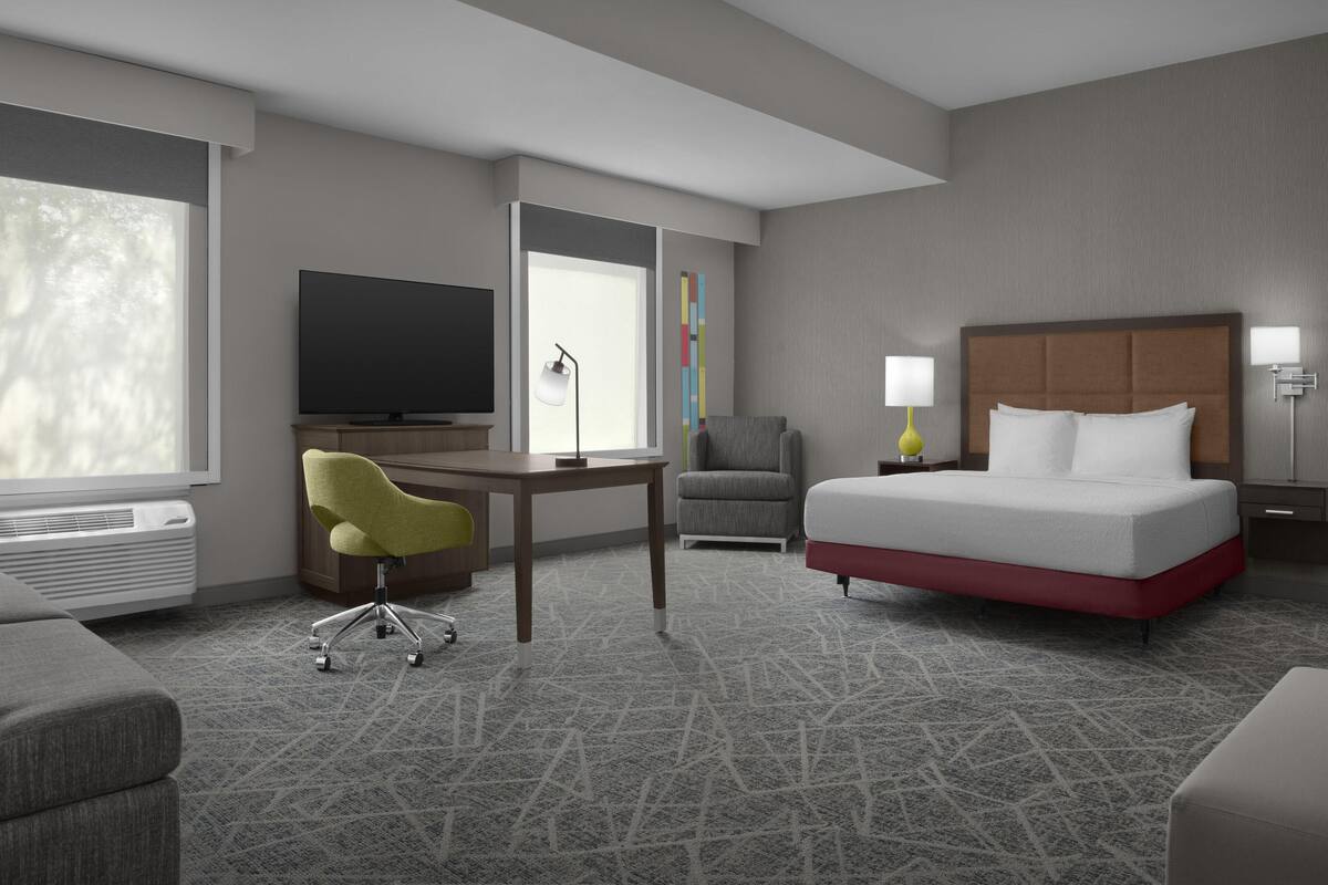 Quarto de hotel com cama, escrivaninha, televisão, poltrona e luminária.