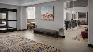 A modern hotel lobby with a bench, a dining area with chairs, a TV, and a colorful rug. - Hampton Inn & Suites Georgetown/Austin North (Georgetown)