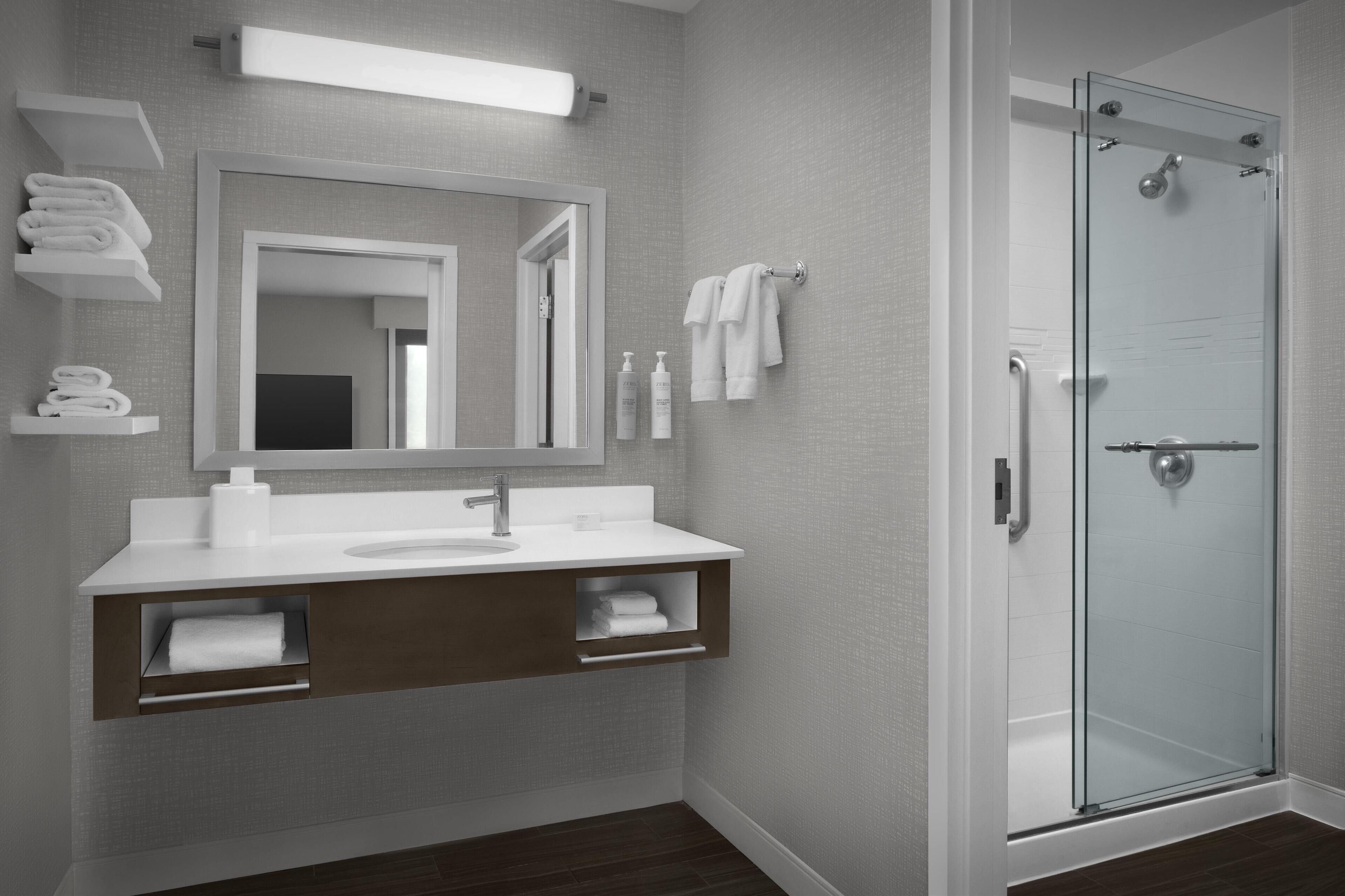 A modern bathroom with a glass shower enclosure, a large mirror, and a white vanity with storage shelves.