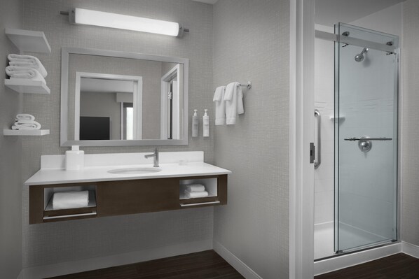 A modern bathroom with a glass shower enclosure, a large mirror, and a white vanity with storage shelves.