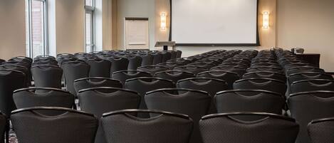 A conference room with rows of black chairs, a projector screen, and a whiteboard.