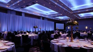 A banquet hall with round tables set for dining, a large screen at the front, and a ceiling with recessed lighting. - Hyatt Place Kansas City/Lenexa City Center (Lenexa)