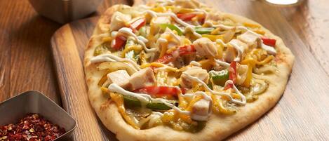 Pizza met diverse toppings op een houten plank, vergezeld van een drankje en een salade op een houten tafel.