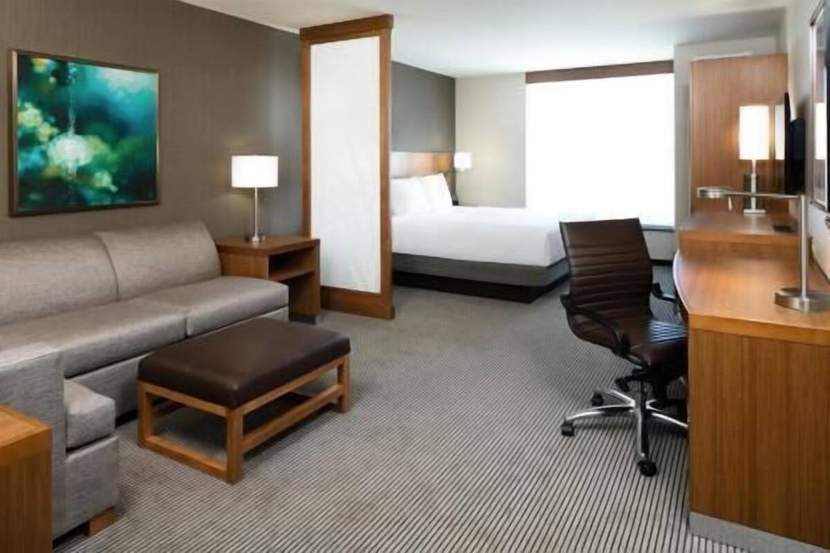 Ein Hotelzimmer mit Bett, Schreibtisch, Stuhl, Sofa, Couchtisch und einem Bild an der Wand.
