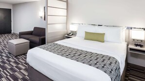 A hotel room with a large bed, a sofa, a small table, and a nightstand with a lamp. - Microtel Inn & Suites by Wyndham West Fargo Medical Center (West Fargo)