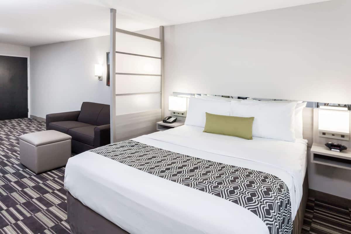 A hotel room with a large bed, a sofa, a small table, and a nightstand with a lamp.