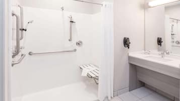 A modern bathroom with a walk-in shower, grab bars, a white sink, and a mirror.