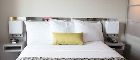 A neatly made bed with white and patterned bedding, a single yellow pillow, and bedside tables with lamps and a telephone.