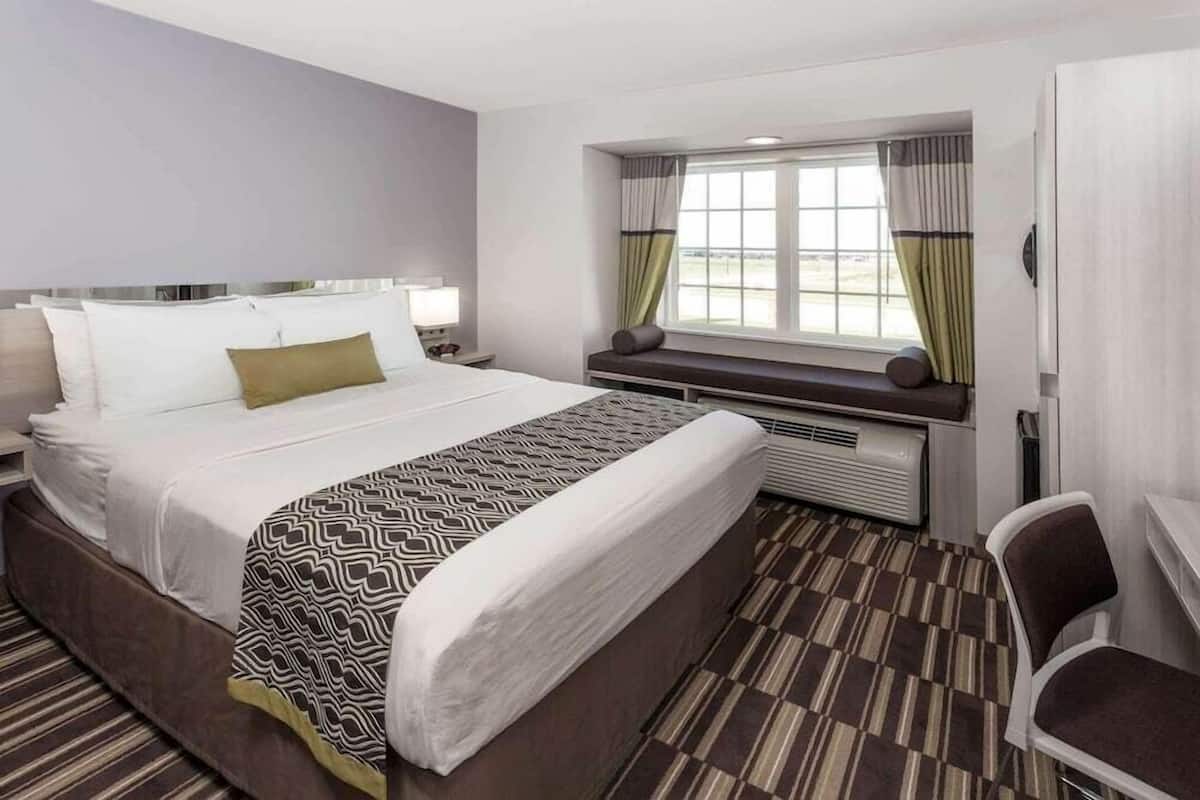 Une chambre d’hôtel avec un grand lit, un bureau, une chaise, une fenêtre avec des rideaux et un appareil de climatisation.