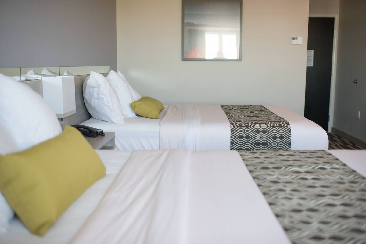 A hotel room with two beds, a bedside table, a mirror, and a door.
