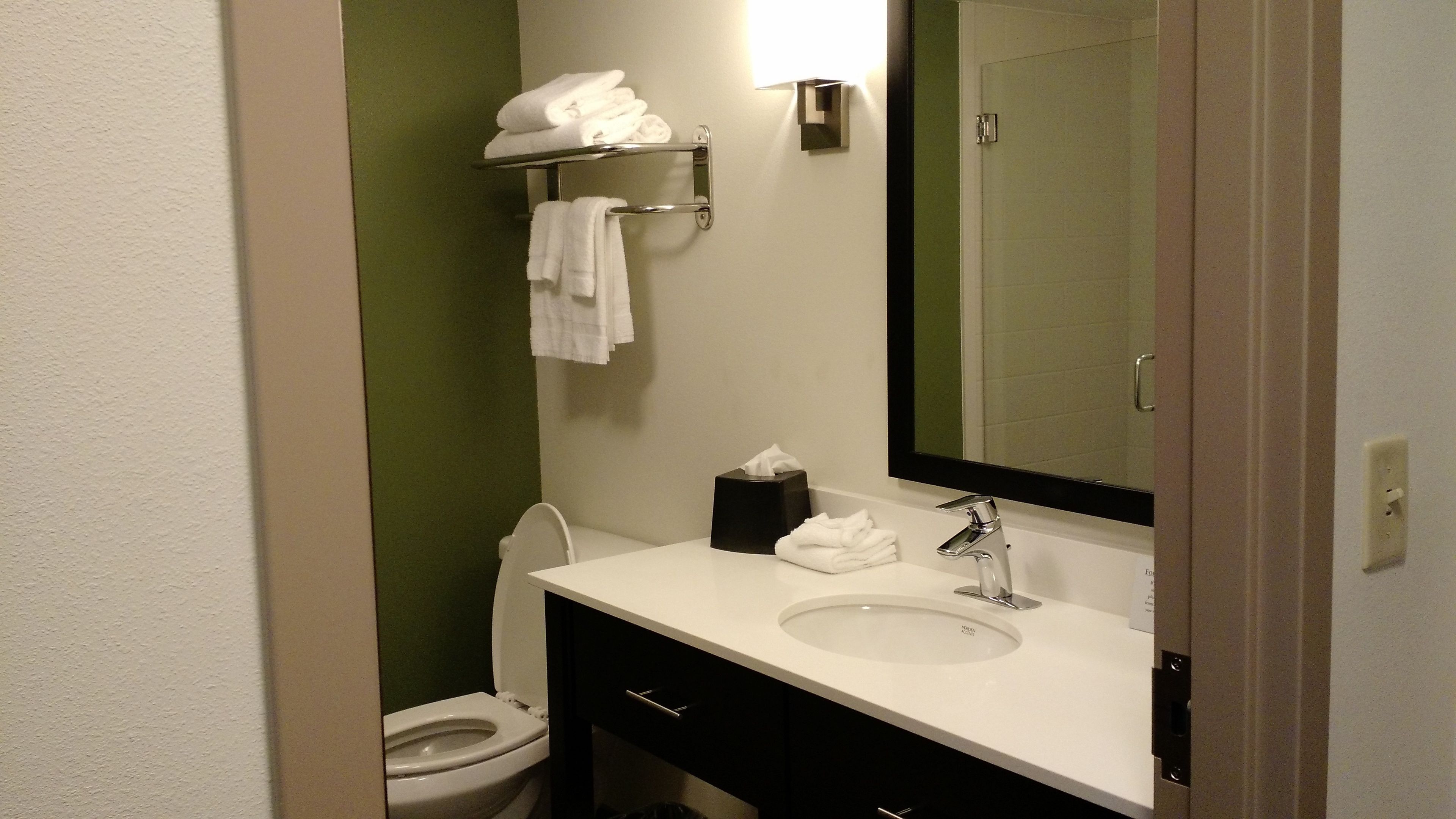 A bathroom with a white sink, a mirror, a towel rack with folded towels, a toilet, and a tissue box.