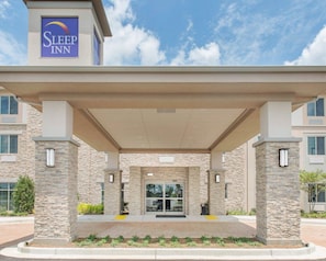 A Sleep Inn hotel entrance with a covered walkway, stone pillars, and a clear sky.