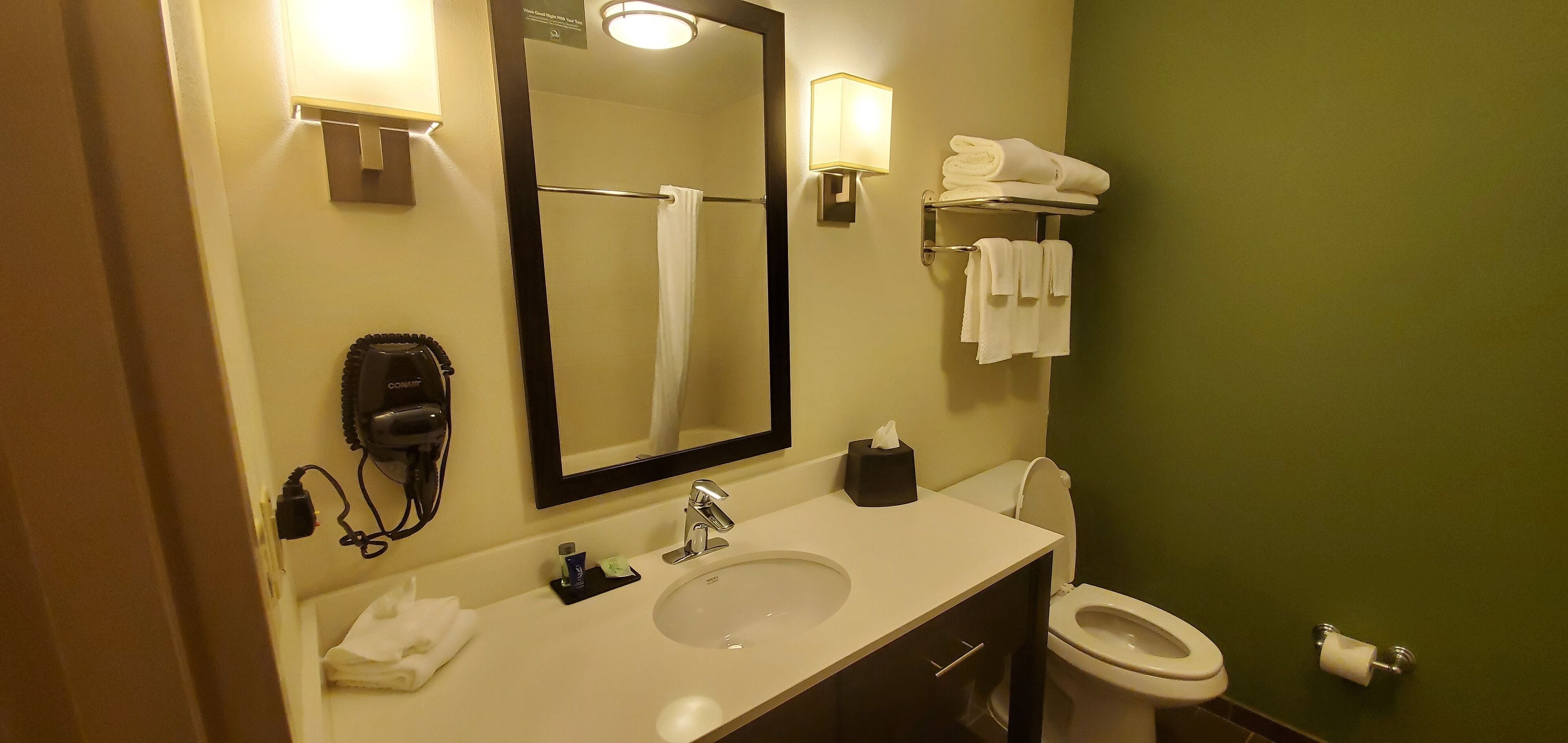 A hotel bathroom with a sink, mirror, towel rack, toilet, and a hairdryer.