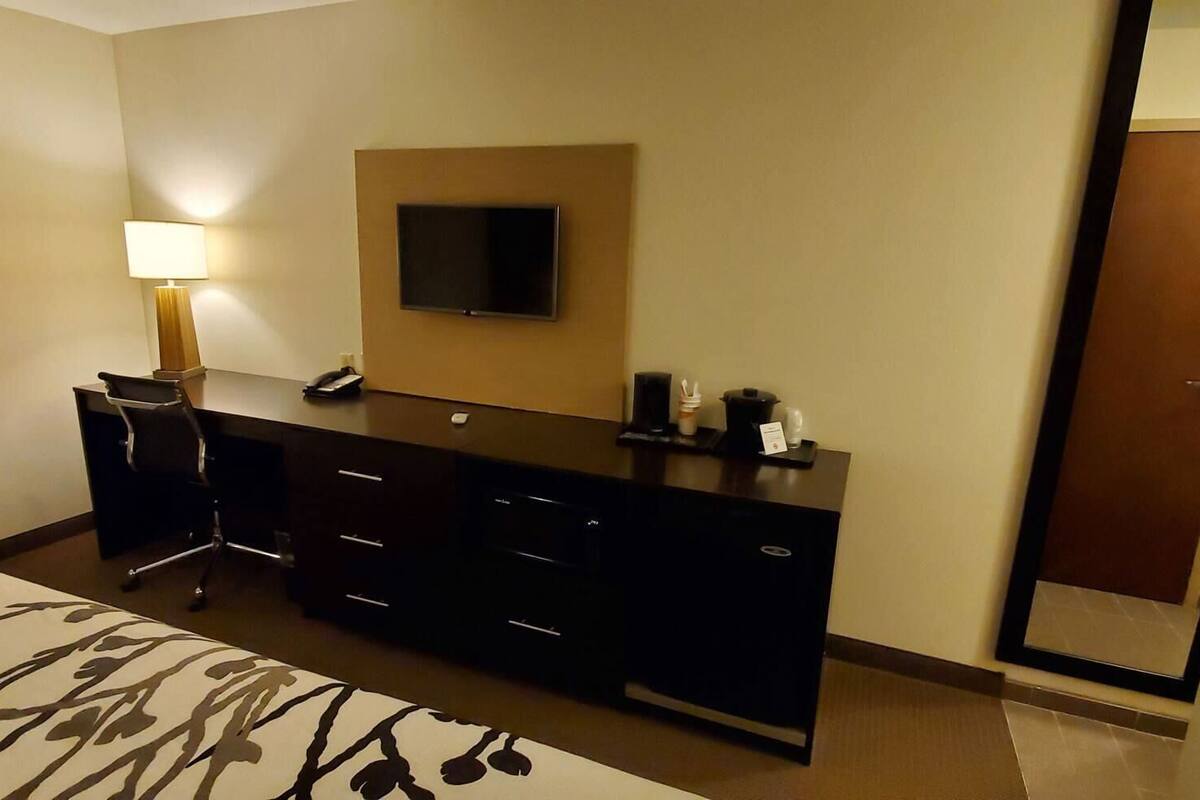 Una habitación de hotel con cama, escritorio, silla, televisor y espejo.