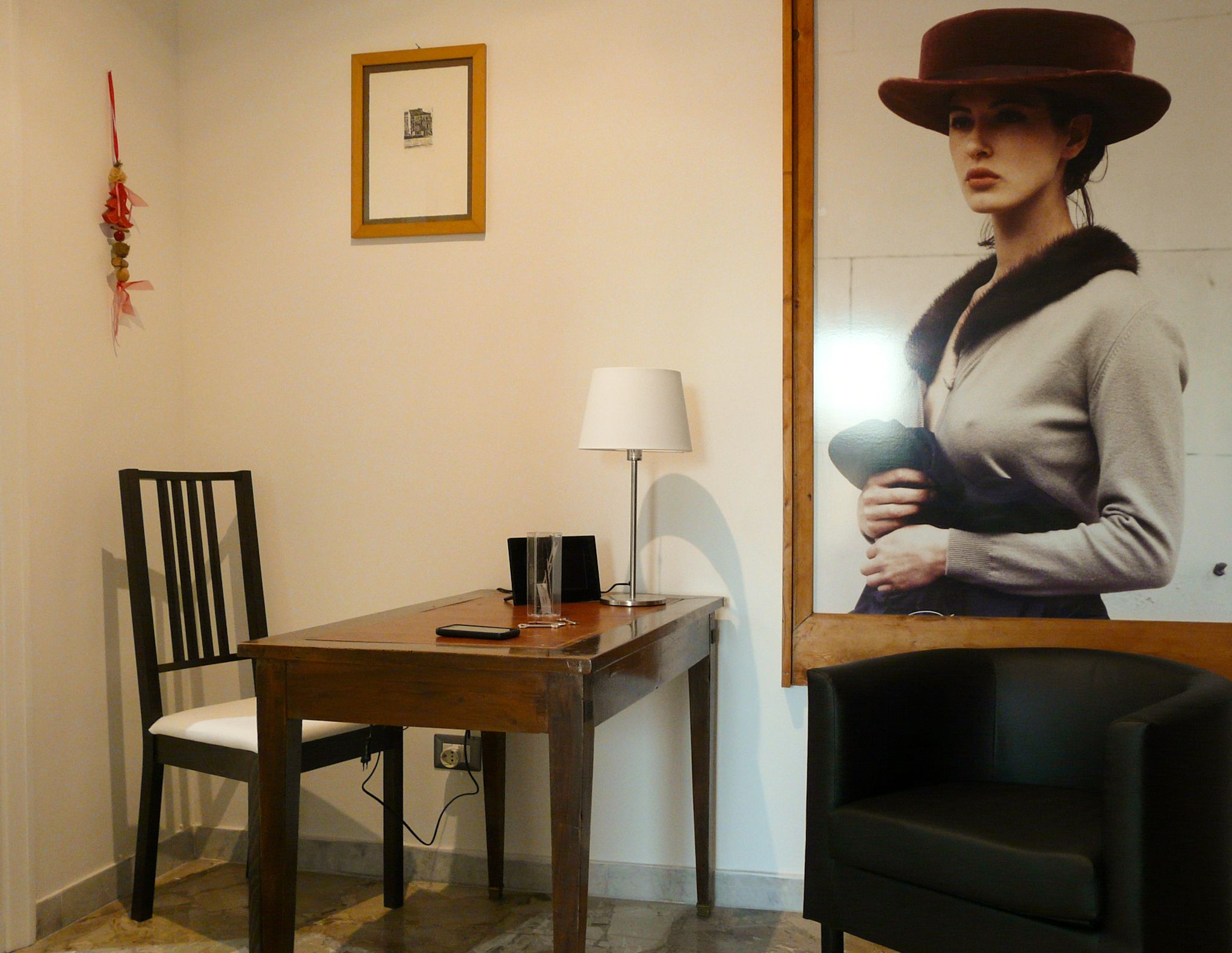 A room with a wooden table, a black chair, a white chair, a lamp, and a framed picture on the wall.