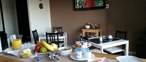 A breakfast setup with fruit, yogurt, and toast on a table, with chairs and a TV in the background.
