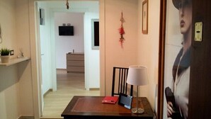 A hallway with a wooden table, a lamp, and a red folder. There is a television in the adjacent room. - Atticoromantica (Rome)