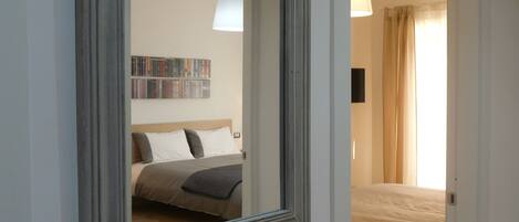 A bedroom with a bed, a bedside table, a lamp, and a wall-mounted shelf with books.