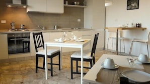 A modern kitchen with white cabinetry, a built-in oven, a dining table with chairs, and a hanging light fixture. - Atticoromantica (Rome)